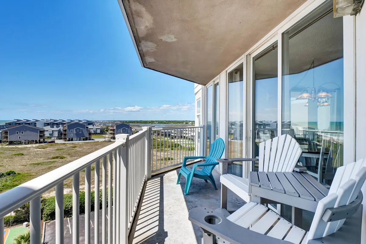 A private balcony set against the backdrop of a sweeping ocean view, with comfortable seating perfect for relaxing. The tranquil scene includes clear blue water, a serene sky, and lush greenery below, conveying a peaceful and romantic ambiance ideal for couples.