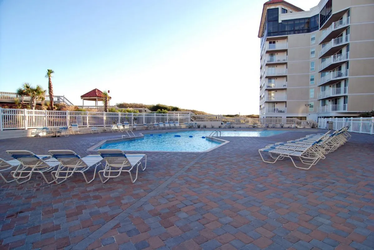 A sunlit swimming pool with lounge chairs and a tastefully landscaped backdrop offers a place for relaxation and play. The pool area invites families to swim, sunbathe, or gather for social activities throughout the year.