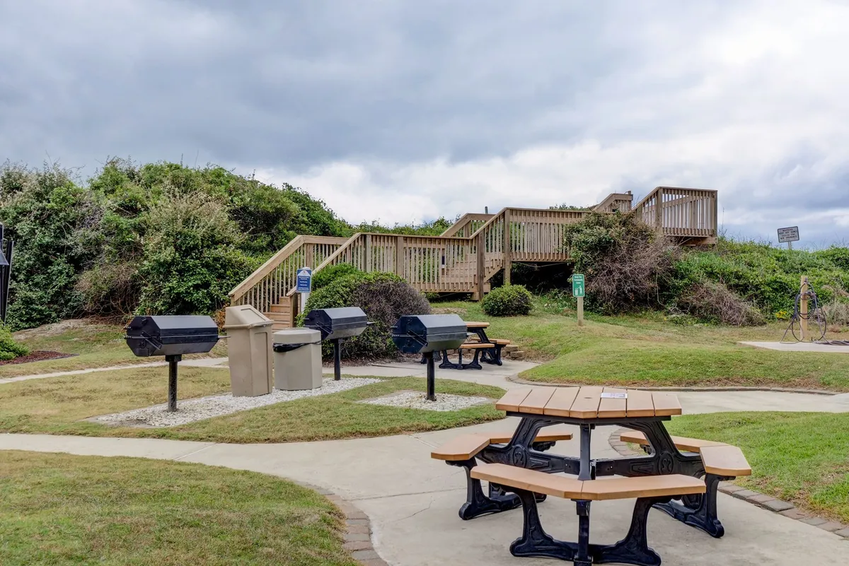 An outdoor grill area with picnic tables, inviting guests to gather for barbecue meals. There is a laid-back, communal vibe, perfect for family cookouts after a day of pool or beach fun.