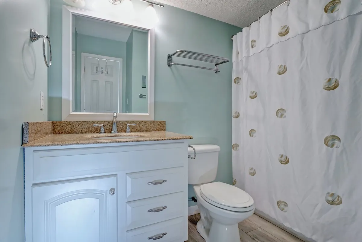 A freshly renovated bathroom with a granite countertop, white cabinetry, a wide mirror, and a stylish shower curtain. The room is bright, clean, and inviting, suggesting a spa-like space for self-care and relaxation.