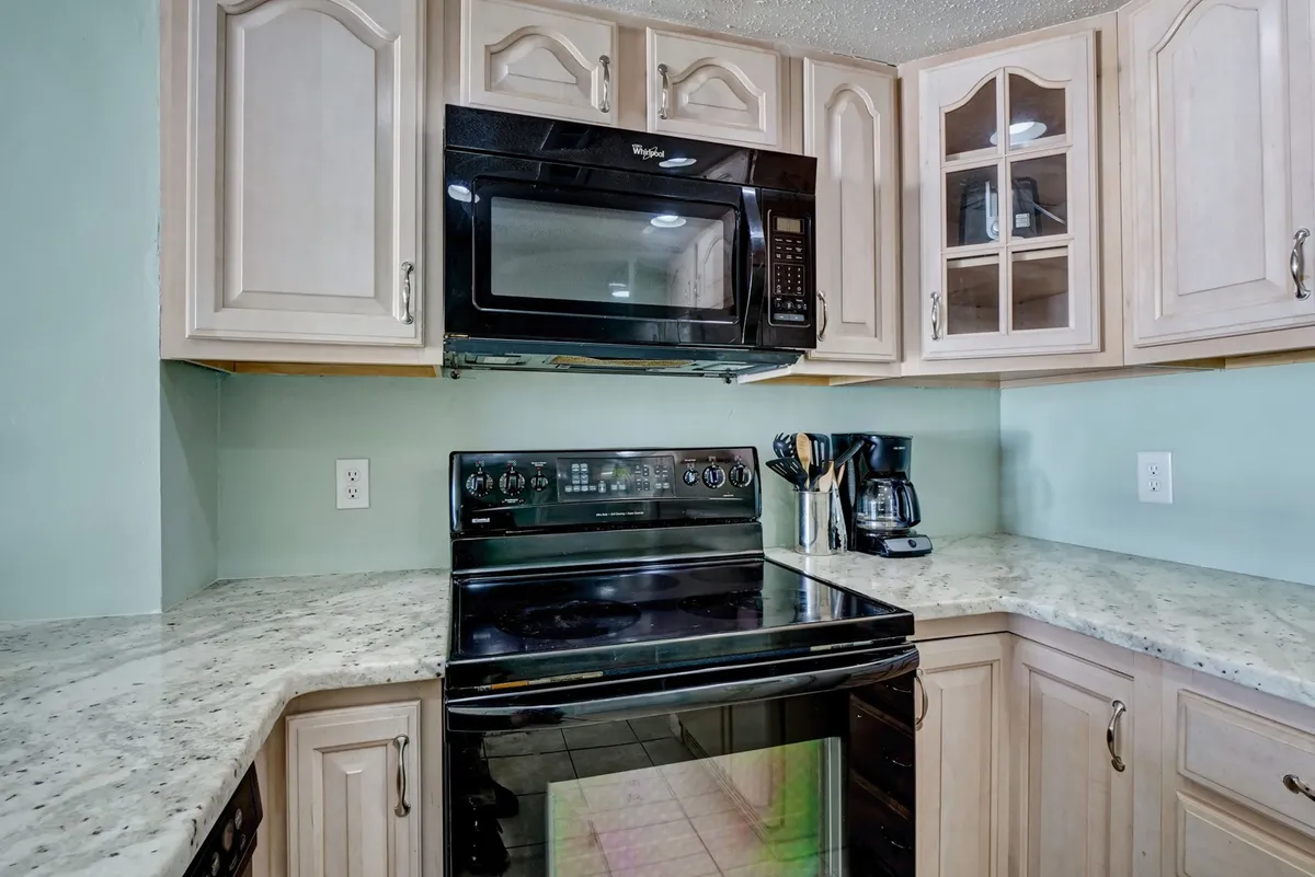 This image highlights a stylish kitchen area featuring black modern appliances, wooden cabinets, a granite countertop, and a coffee maker. The warm cabinetry and sleek finishes evoke a welcoming and functional cooking environment.