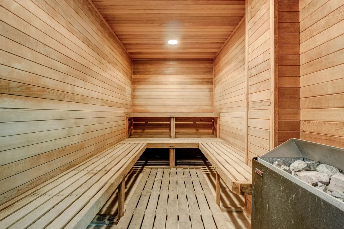 A peaceful sauna room with wooden benches and a central stone heater, bathed in warm, calming light. The space is inviting and clearly meant for relaxation, inviting guests to unwind and enjoy a couples' spa experience.