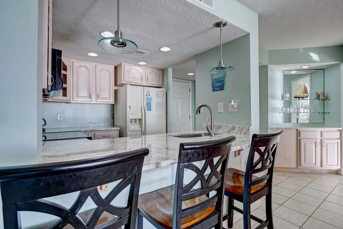 The image features a spacious kitchen island with bar stools, striking granite countertops, and plentiful cabinetry. The open layout encourages both meal preparation and social gatherings, in line with the 'Chef’s Corner' narrative.